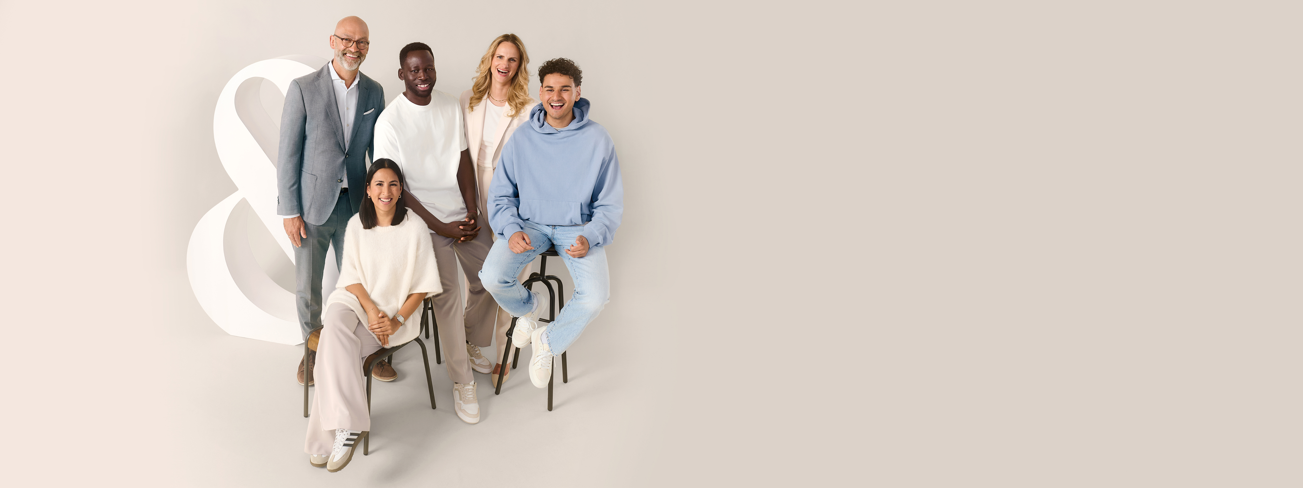 Eine Gruppe Menschen verschiedenen Alters und Geschlechts stehen vor einem beigen Hintergrund neben einem "Et-Zeichen".